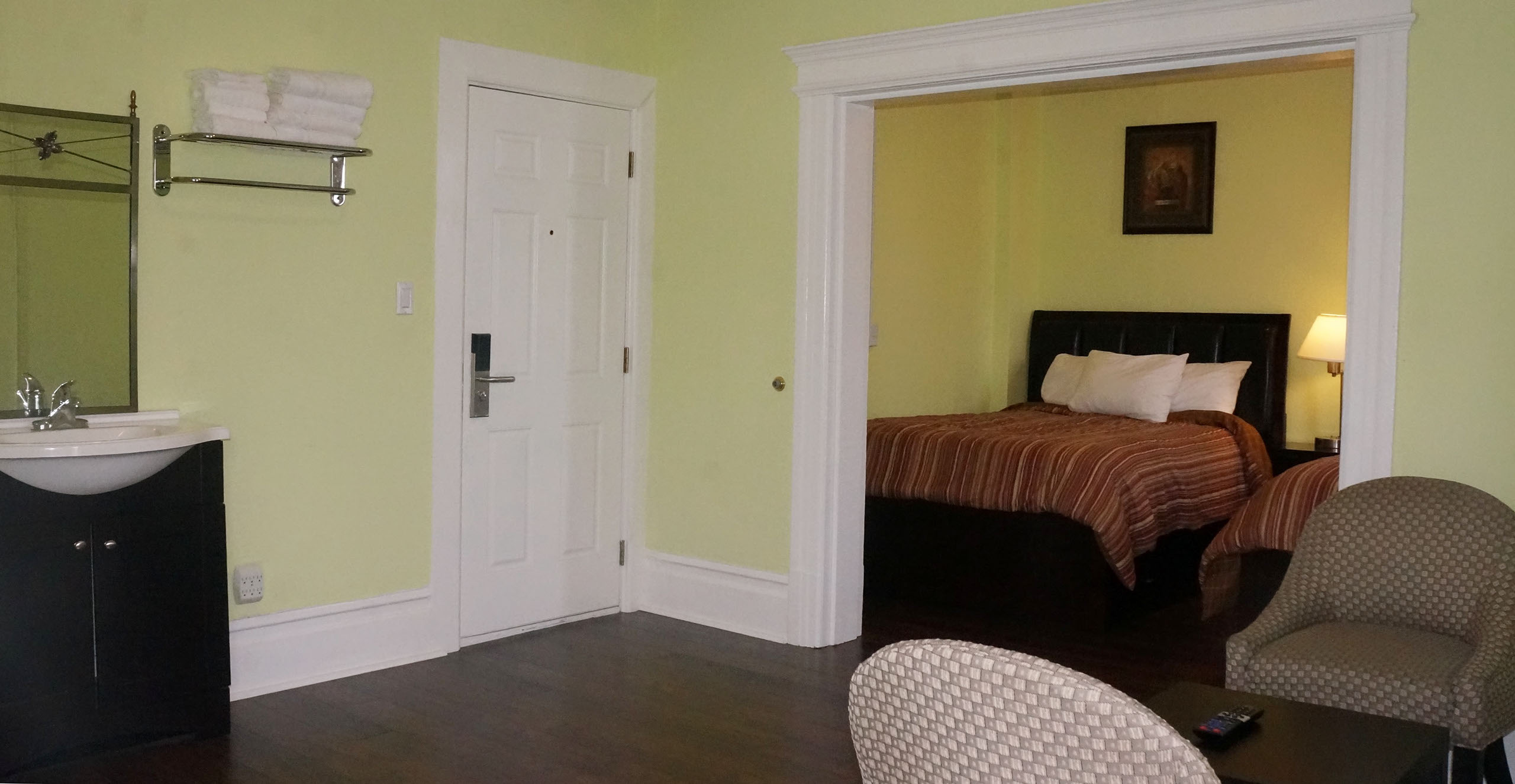 A hotel room with a bed, sink, mirror, chair, and doorway.