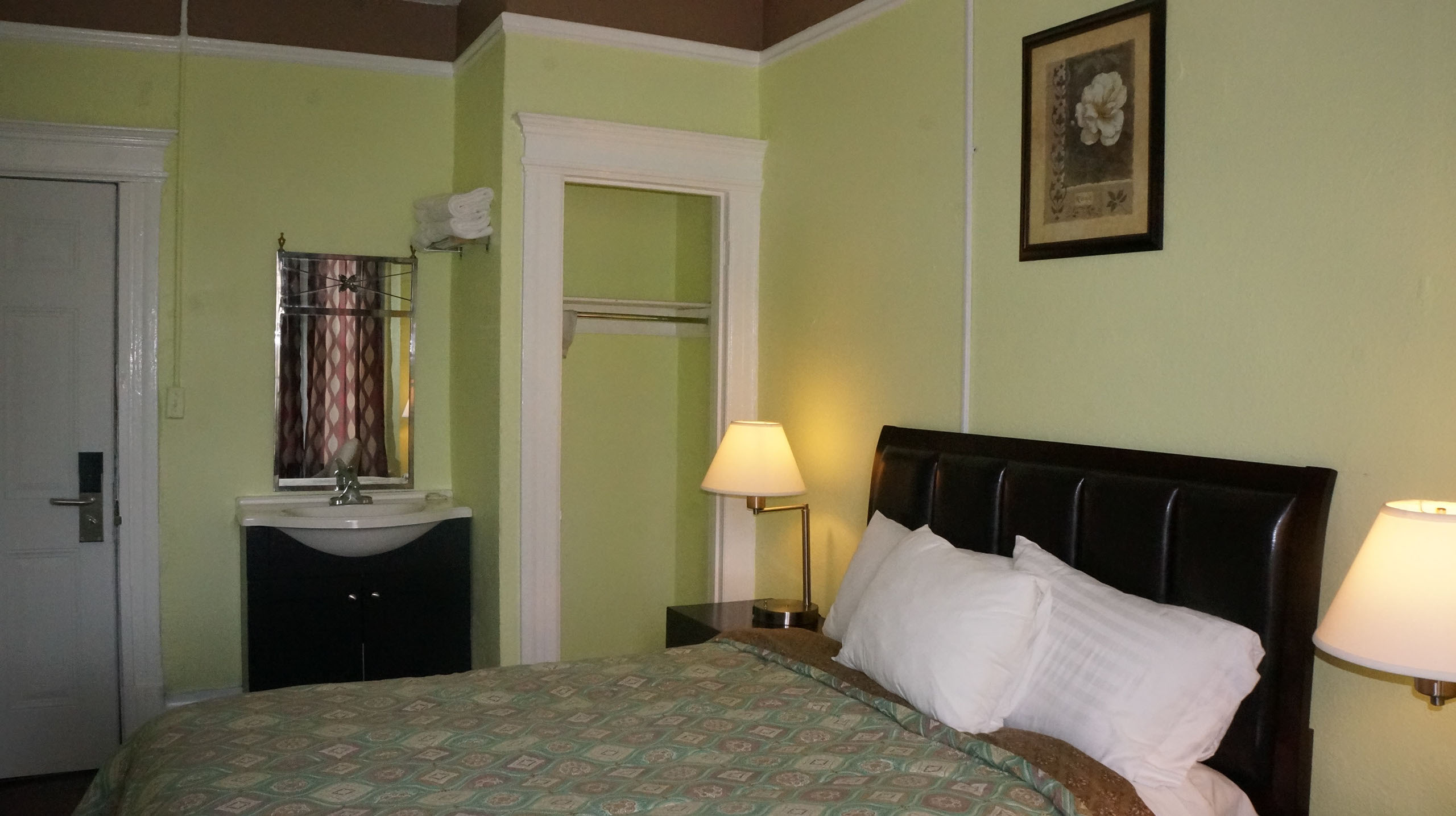 A hotel room with a bed, nightstand, closet, and sink